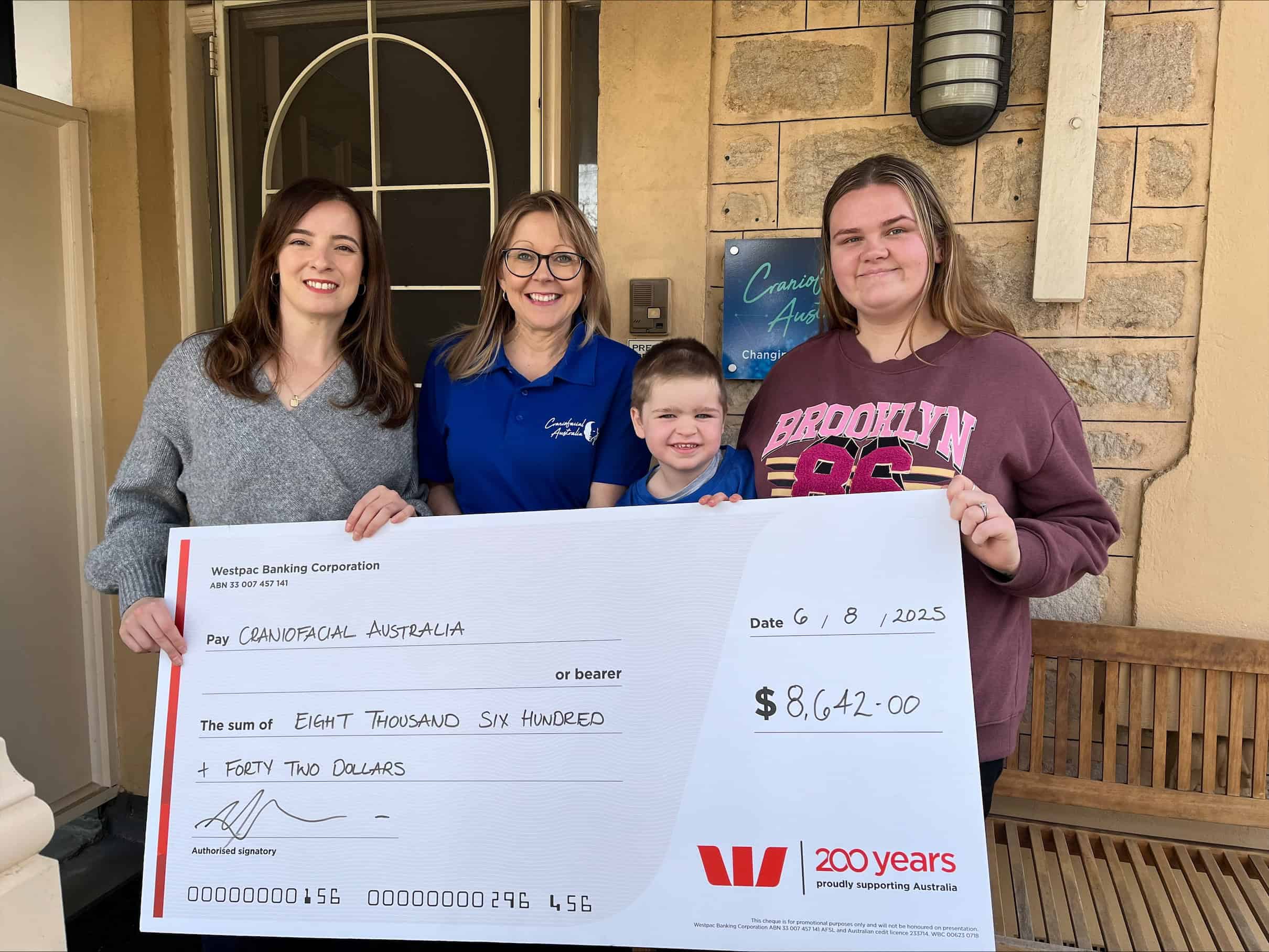 Family holding a large cheque for craniofacial support in Australia.