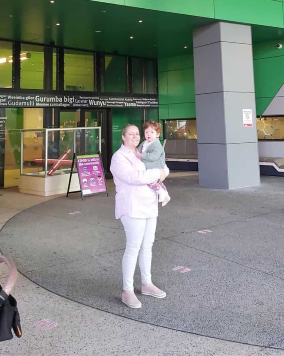 Baby with Hypoxic Ischemic Encephalopathy and Unicoronal synostosis held by his mother, standing outside of hospital