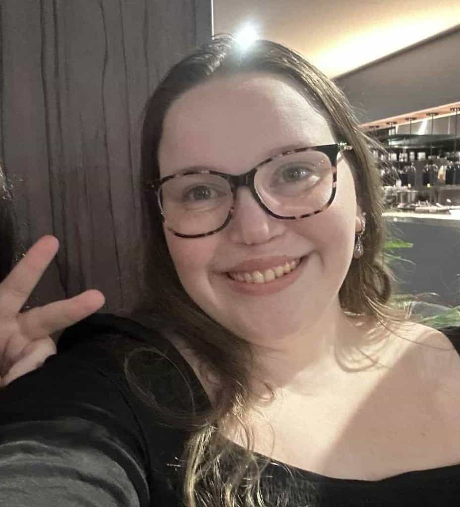 Young woman with cleft lip and palate smiling, making a peace sign at a craniofacial support event in Australia.