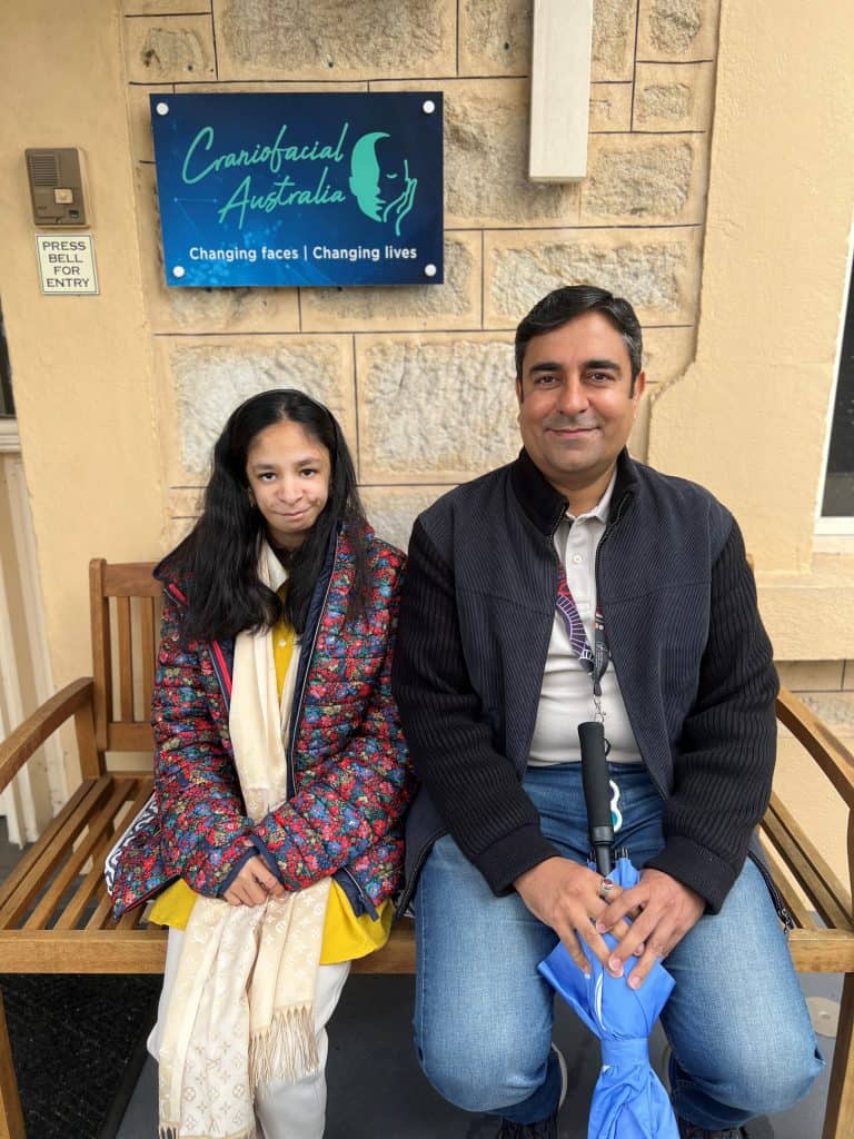 Girl with Nager Syndrome and her father sitting on a bench at the front of the Craniofacial Australia office.