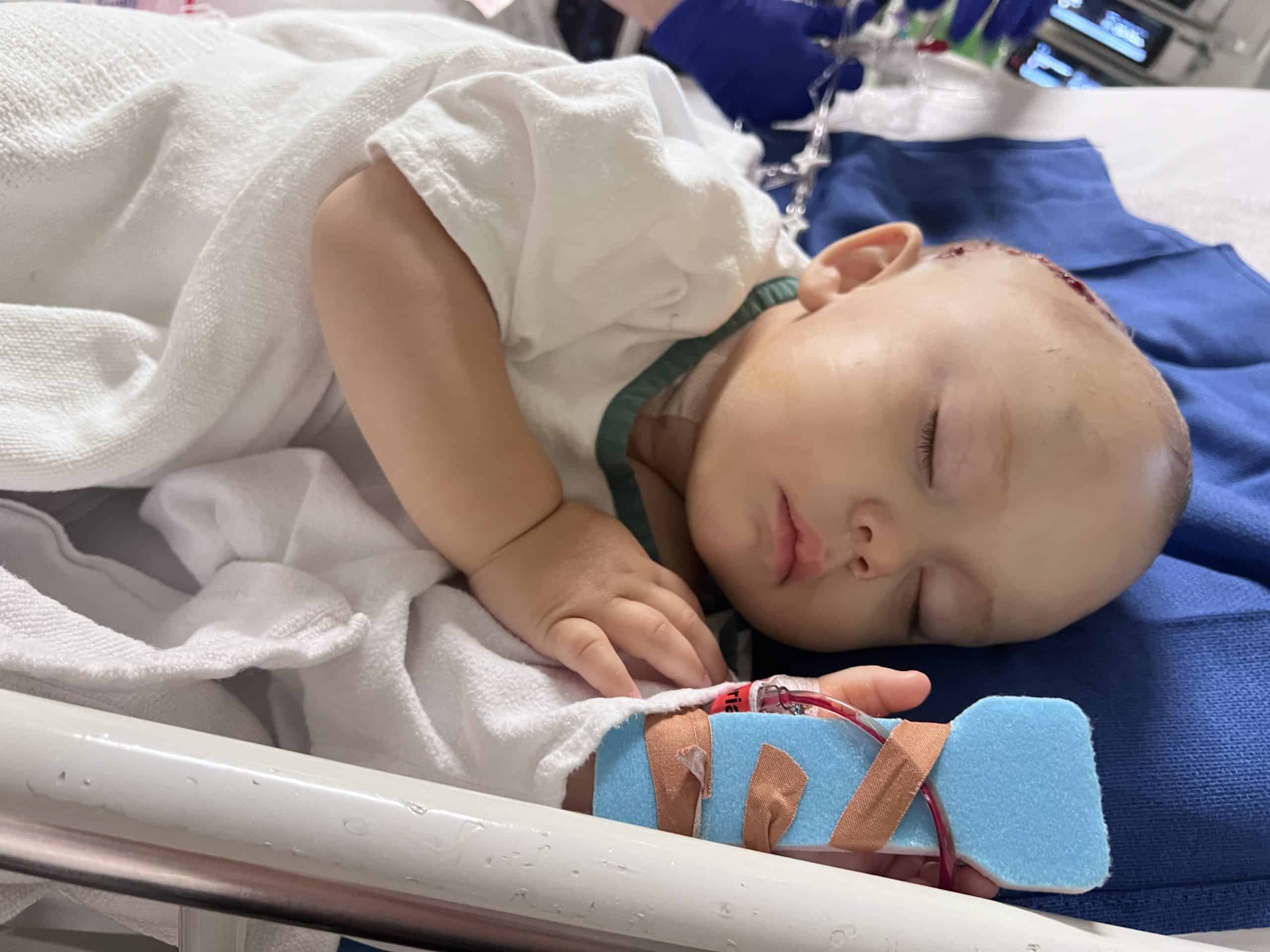 A child sleeping peacefully in a hospital bed with medical tubes and equipment.