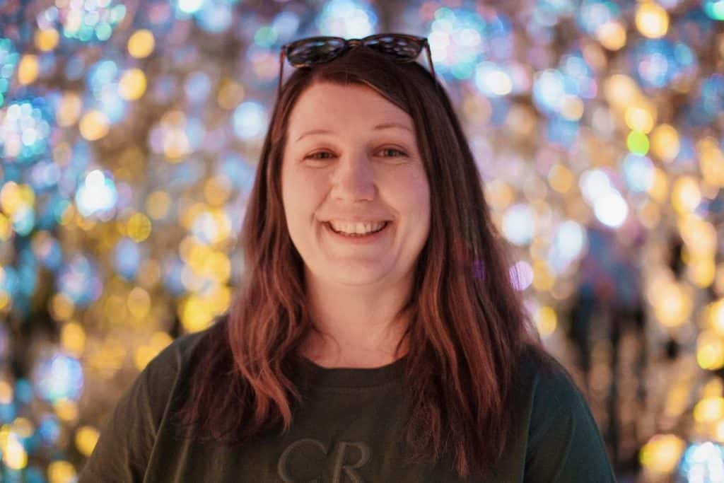 A smiling woman with long brown hair and sunglasses on her head, festive background.