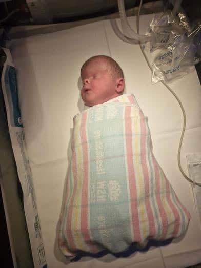 Newborn baby wrapped in hospital blanket in neonatal intensive care unit.