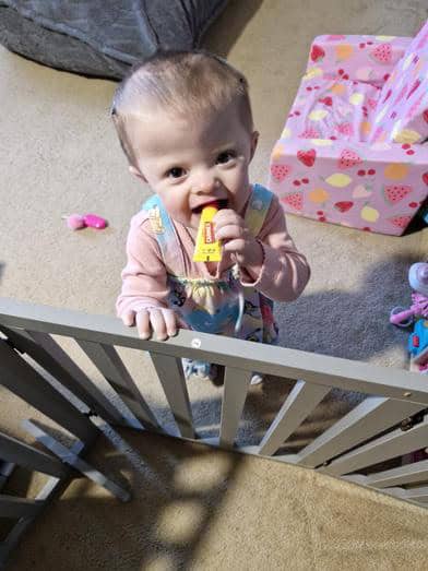 Young child with a pacifier in a playpen, surrounded by toys and gifts.