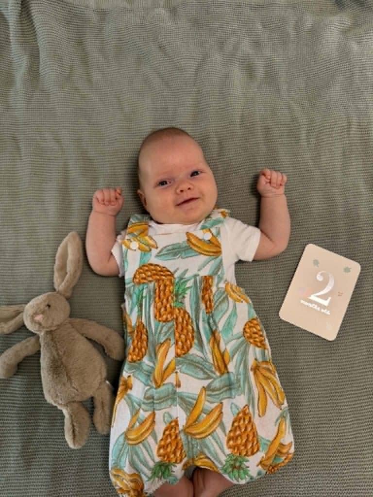 Adorable baby lying on a grey blanket with a plush bunny and a 2nd birthday card.
