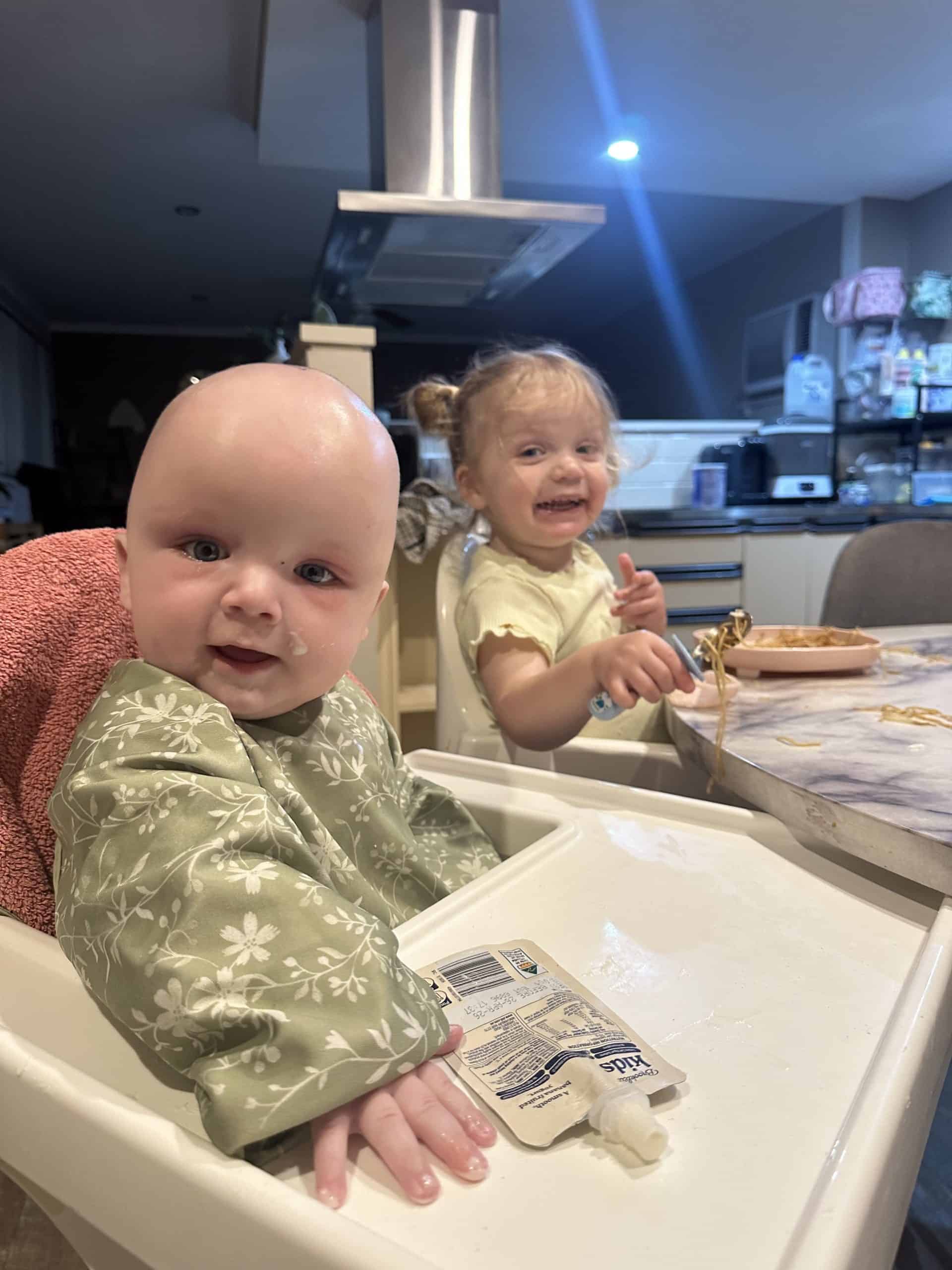 Two young children sitting at a dining table, smiling and enjoying a meal.