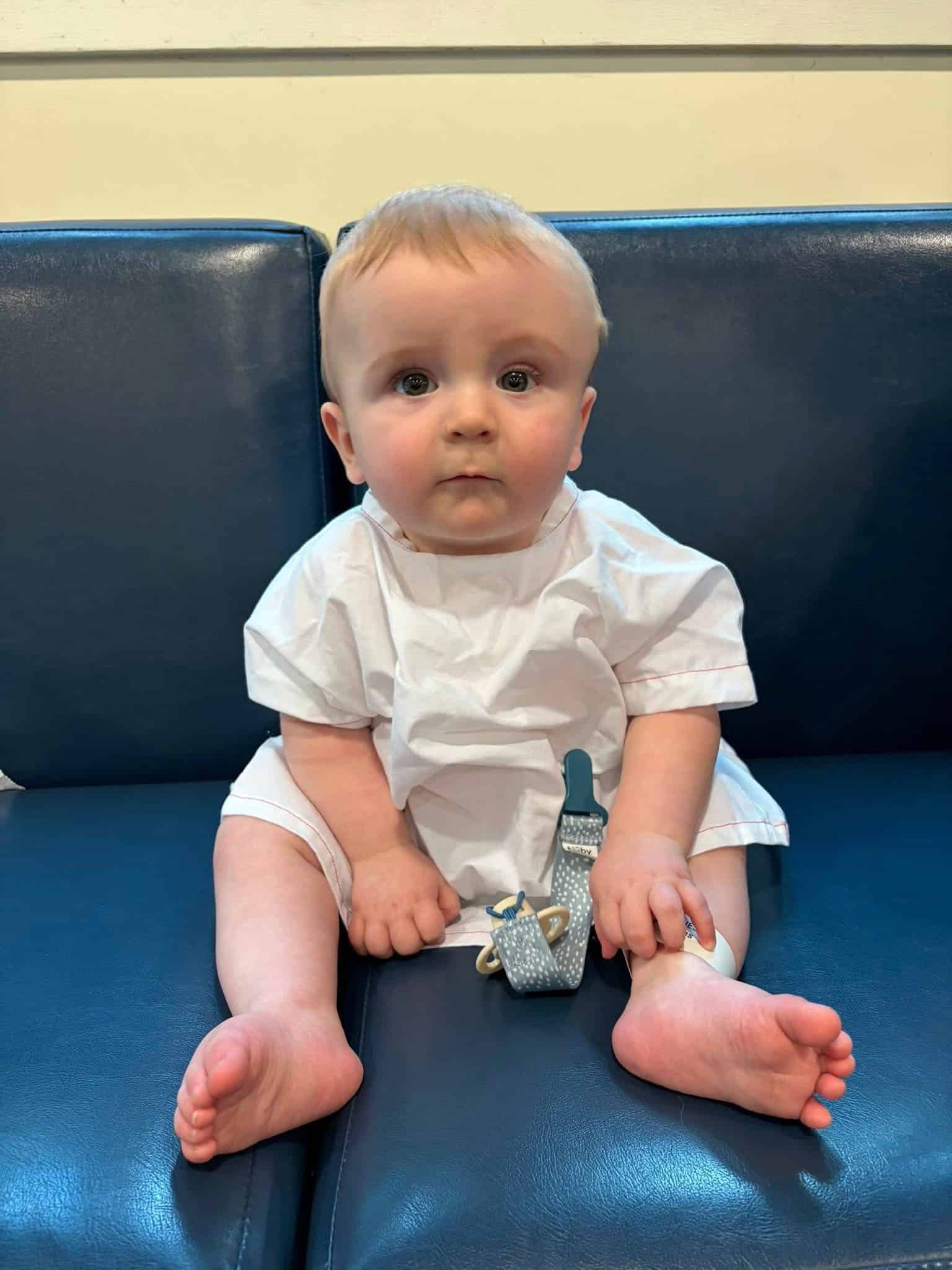 Adorable young child with medical bandage on foot sitting on a blue couch.