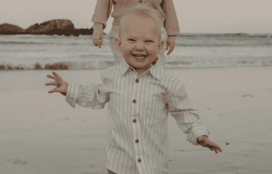 Happy young child playing on the beach with ocean in background.